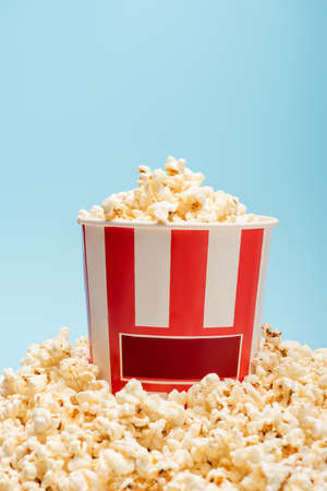 striped bucket and pile of tasty popcorn isolated on blue, cinema conceptの写真素材