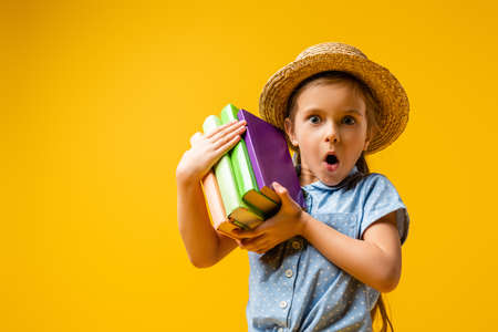 surprised girl in straw hat holding books isolated on yellowの写真素材