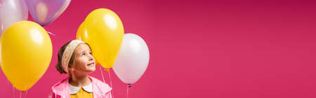happy kid looking away near balloons isolated on crimson, bannerの写真素材