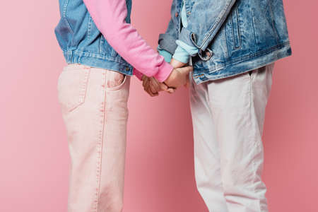 Cropped view of teen couple holding hands on pink backgroundの写真素材