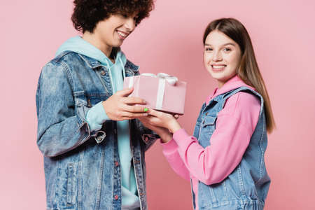 Smiling teenager giving present to girlfriend on pink backgroundの写真素材