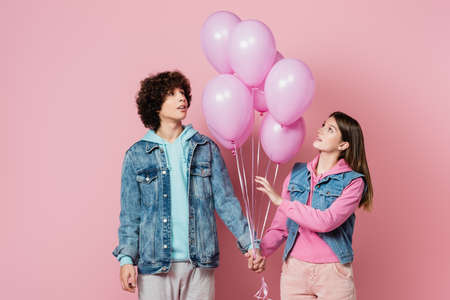 Teenagers holding hands while looking at balloons on pink backgroundの写真素材