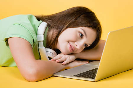 Smiling teenage girl looking at laptop on yellow background