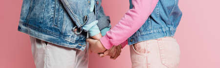 Cropped view of teenagers in denim jackets holding hands on pink background, bannerの写真素材