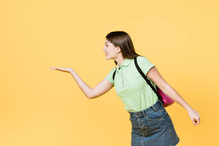 Smiling teen girl with backpack pointing with hand isolated on yellowの写真素材