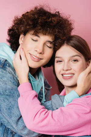 Cheerful teenagers touching faces of each other on pink background