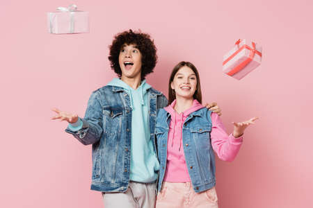 Cheerful teen couple embracing near presents isolated on pinkの写真素材