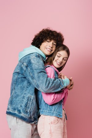 Side view of curly teenager embracing girlfriend on pink backgroundの写真素材