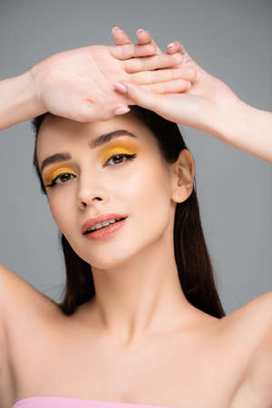 brunette young woman with yellow eyeshadow looking at camera isolated on grayの写真素材