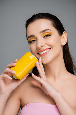 happy young woman holding yellow can with soft drink isolated on gray