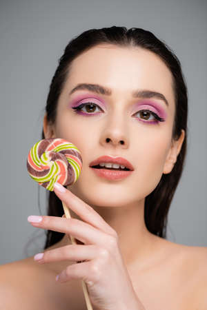 young woman with pink eye shadows holding lollipop isolated on grayの写真素材