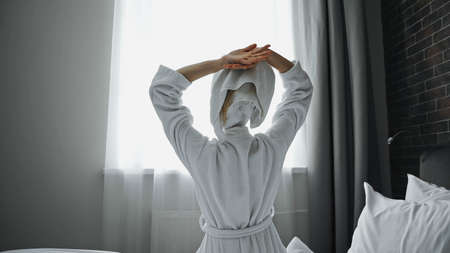 back view of woman in bathrobe stretching in hotel roomの写真素材