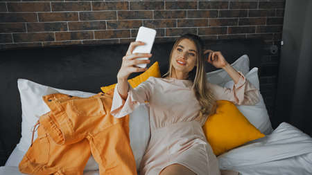 cheerful woman taking selfie on bed in hotel room