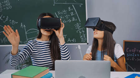 mother and daughter in vr headsets near laptop and books on deskの写真素材
