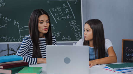 mother and daughter doing homework near laptop and notebooks on table