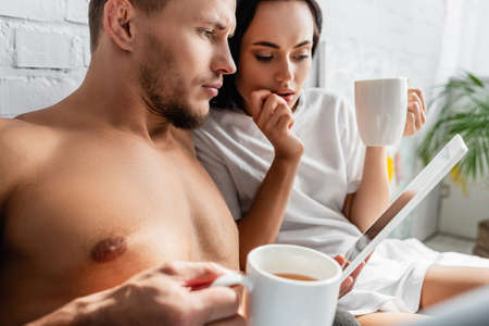 Shirtless man holding digital tablet near girlfriend with cup on blurred backgroundの写真素材