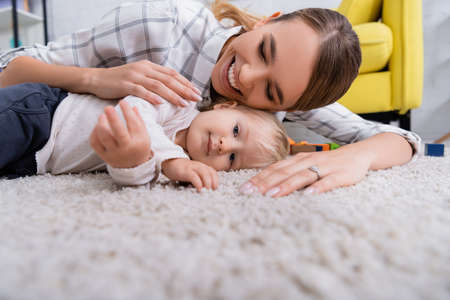 surface level of happy mother with little son lying on carpet at home, blurred foregroundの写真素材