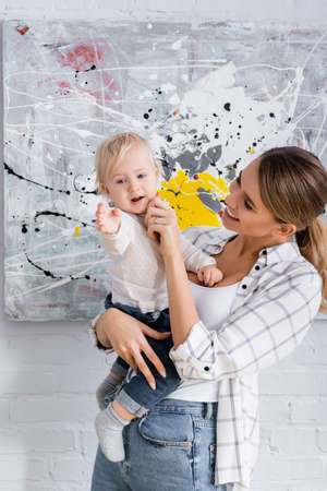 smiling mother touching cheek of little son while holding him at homeの写真素材