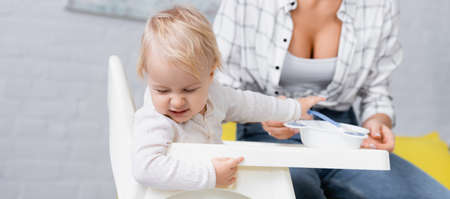 frowning child turning away from food near mother on blurred background, banner