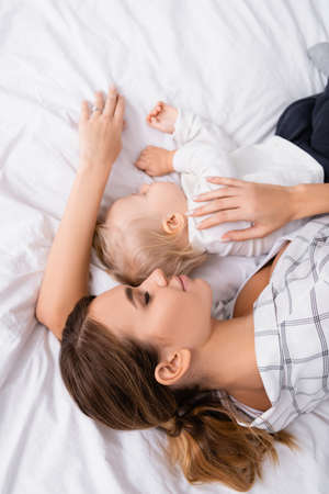 top view of young mother with toddler son sleeping on white bedding