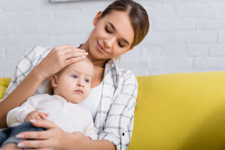 smiling mother embracing toddler son looking away at homeの写真素材