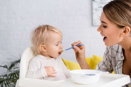young woman with open mouth feeding toddler son at home