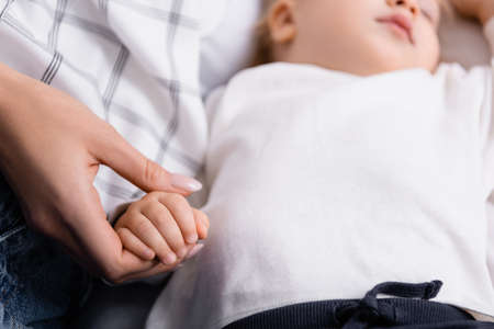 cropped view of mother holding hand of sleeping baby boy, blurred backgroundの写真素材