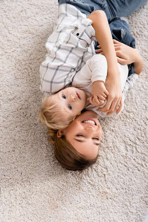 overhead view of joyful woman embracing son while lying on floor togetherの写真素材