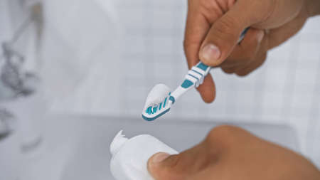 partial view of man applying toothpaste on toothbrush in bathroom
