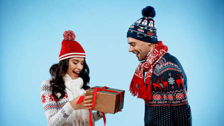 Smiling man in sweater standing near girlfriend with present on blue background
