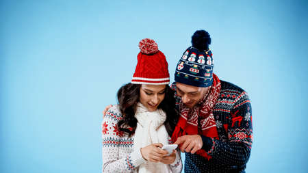 Smiling couple in warm clothes using smartphone on blue backgroundの写真素材
