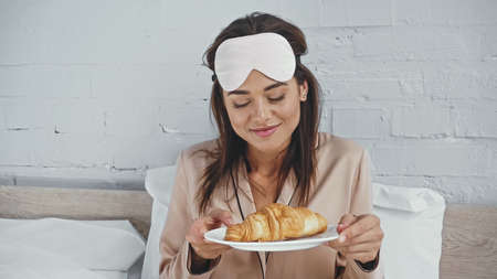 happy woman with eye mask holding plate with tasty croissantの写真素材