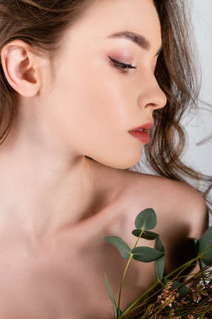 Young model with naked shoulder looking at flowers isolated on grayの写真素材