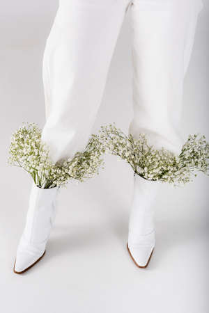 Cropped view of baby breath flowers in shoes of woman on gray background