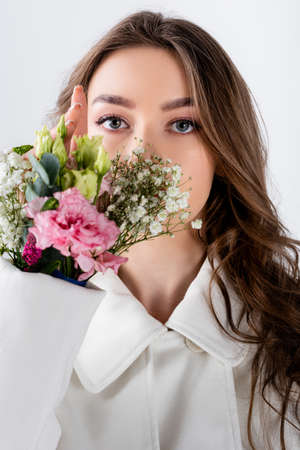 Brunette woman looking at camera near flowers in sleeve of coat isolated on grayの写真素材