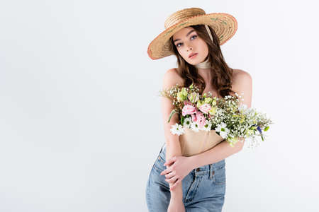 Woman with flowers in blouse posing in straw hat isolated on grayの写真素材