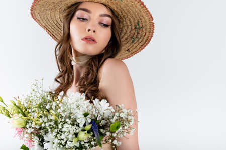 Brunette woman in sun hat looking away near bouquet isolated on grayの写真素材
