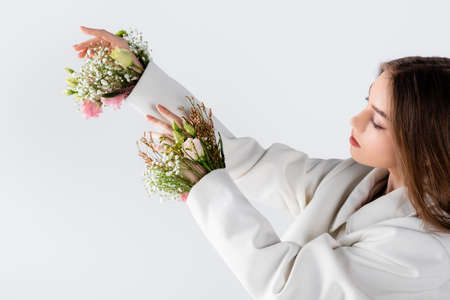 Woman looking at flowers in sleeves of blazer isolated on grayの写真素材