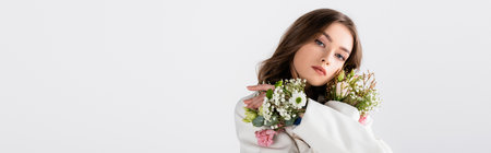 Brunette woman posing with flowers in sleeves isolated on gray, banner