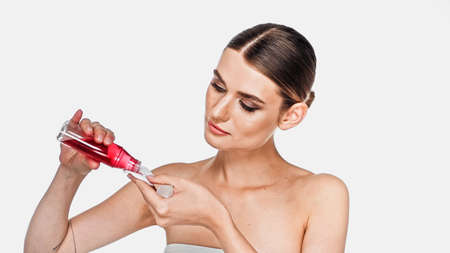 Young adult woman pouring tonic on cotton pad isolated on whiteの写真素材
