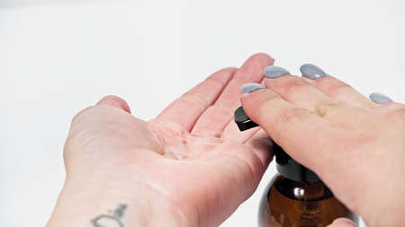Cropped view of woman squeezing liquid in cosmetic bottle on white