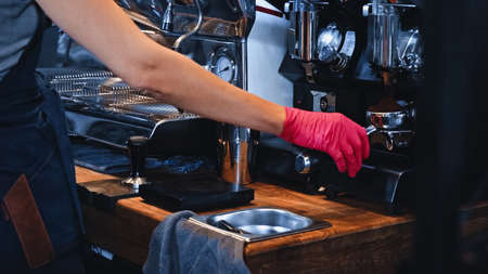 cropped view of barista in latex glove holding portafilter with ground coffee in coffee shopの写真素材