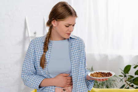 Upset woman with allergy looking at plate with nutsの写真素材