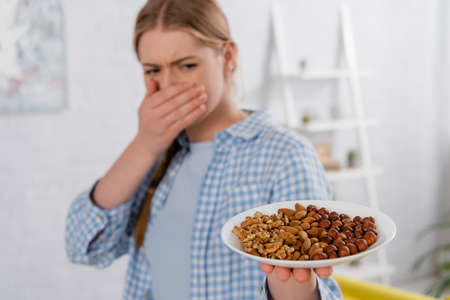 Plate with nuts in hand of woman with allergy on blurred backgroundの写真素材