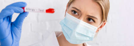 Doctor in medical mask holding test tube with blood sample during allergy test on blurred...