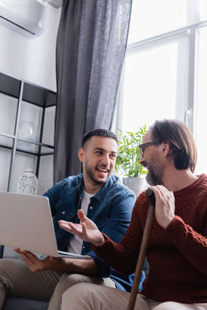 bearded man with walking stick pointing at laptop near excited hispanic sonの写真素材