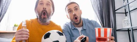 excited interracial father and son watching football championship at home, banner