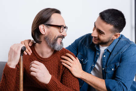 smiling hispanic man hugging shoulders of happy father at homeの写真素材