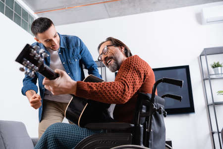 low angle view of cheerful disabled man playing guitar near excited hispanic sonの写真素材