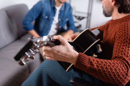 partial view of disabled man playing acoustic guitar near son on blurred backgroundの写真素材